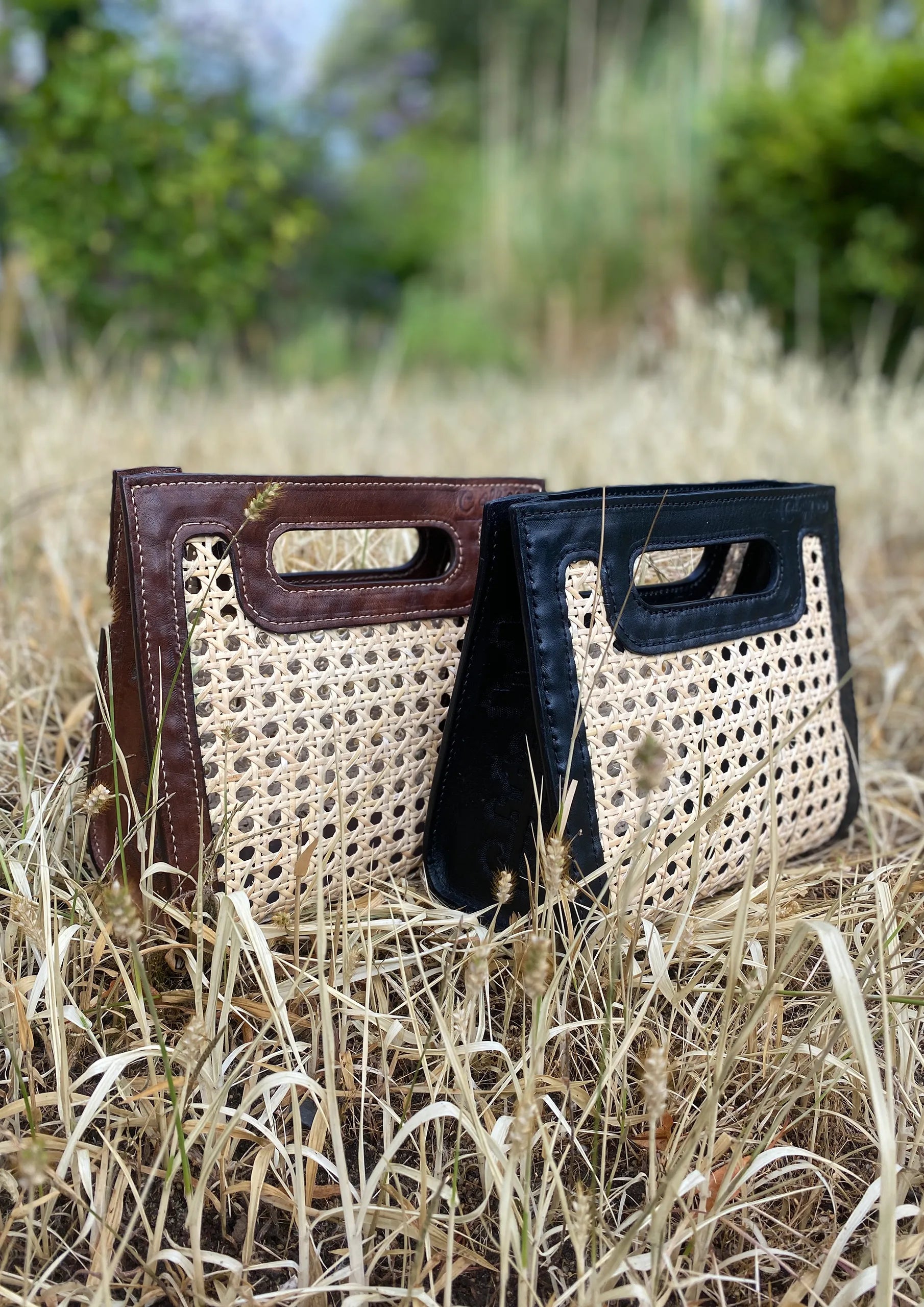 Bolsos Coffe Coccon hechos de hojas de palma de iraca naturales marrones y negras tejidos a mano se ubican sobre pasto seco, uno al lado del otro